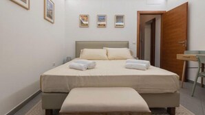 A bedroom with a bed, bedside tables, a bench, and a door. - Cozy apartment in the heart and historic center of Palermo. (Palermo)