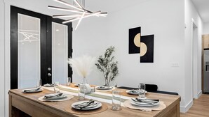 Zona pranzo con tavolo in legno apparecchiata per quattro persone, lampada a sospensione moderna e arredamento minimalista che include un vaso con piante e arte astratta alle pareti.
