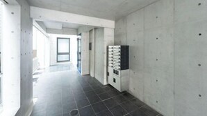 A hallway with a tiled floor, concrete walls, and a row of lockers on the right. - Ferio Kamata II (Tokyo)