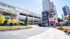 A modern urban street with a multi-level parking structure, a mix of commercial buildings, and a clear sky. - Ferio Kamata II (Tokyo)