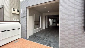 A hallway with grey tiled walls and a tiled floor, leading to a room with a window and a door. - Ferio Kamata II (Tokyo)