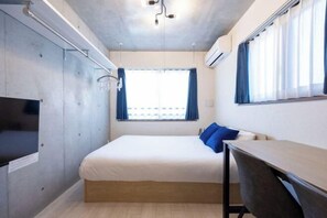 Ein gemütliches Zimmer mit Bett, Schreibtisch, Fernseher und einem fensterbepflanzten Fenster.