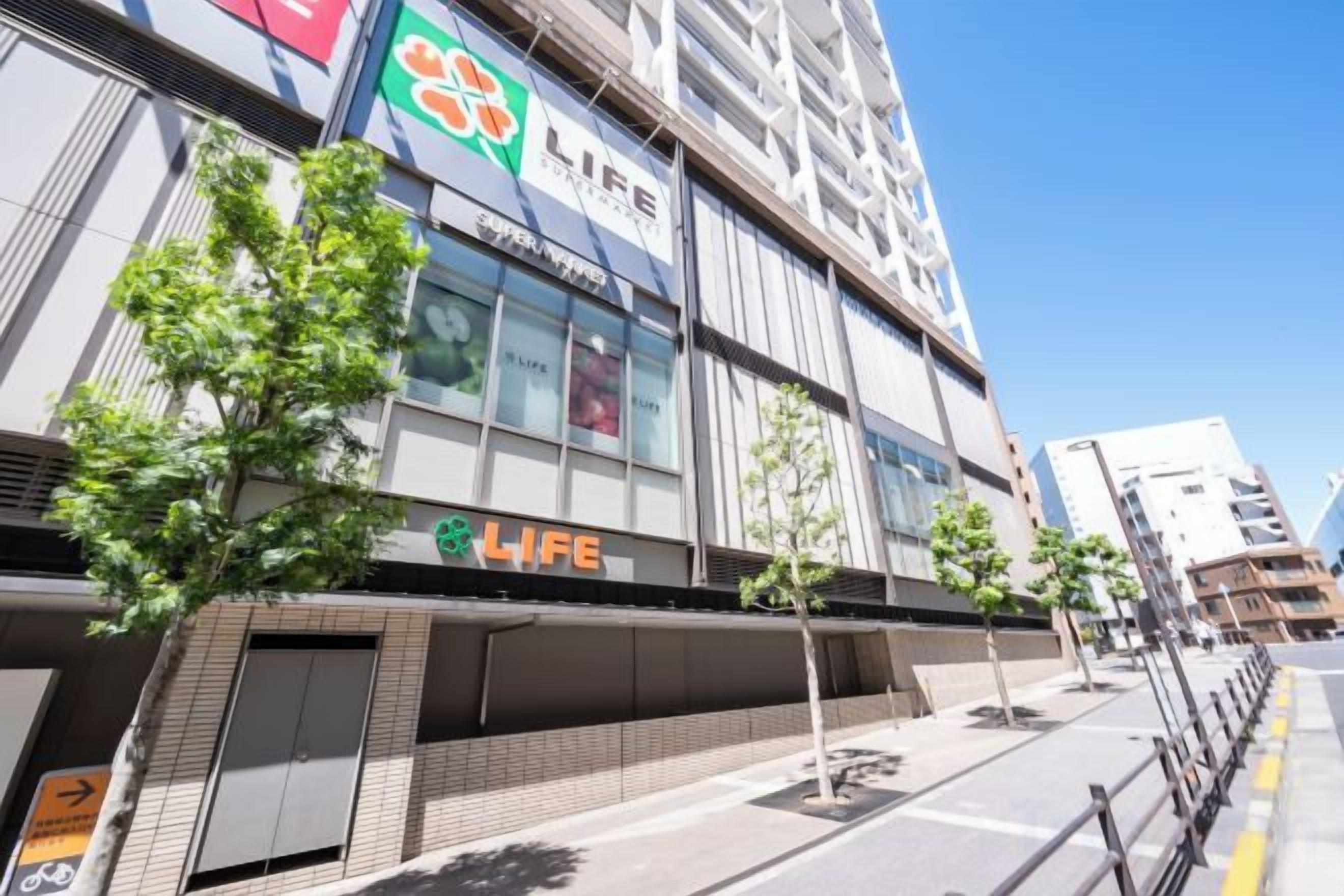 Um edifício com vários andares, um destaque com a placa 'LIFE', uma entrada coberta e céu claro.