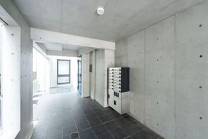 A hallway with a tiled floor, concrete walls, and a door at the end. - Ferio Kamata II (Tokyo)