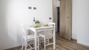 A small dining area with a white table and chairs, a bottle, and a small plant. - Profumo di Caruggi - Room Porto Antico (Genova)