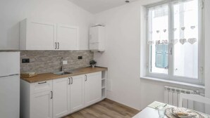 A modern kitchen with white cabinets, a wooden countertop, and a window with heart-shaped decorations. - Profumo di Caruggi - Room Porto Antico (Genova)