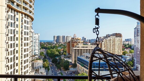 A balcony with a hanging chair, a view of a cityscape, and a building with balconies. - Rodos Arcadia Apartments (Odesa)