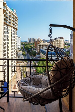 A balcony with a hanging chair, a view of a cityscape, and a building with balconies. - Rodos Arcadia Apartments (Odesa)
