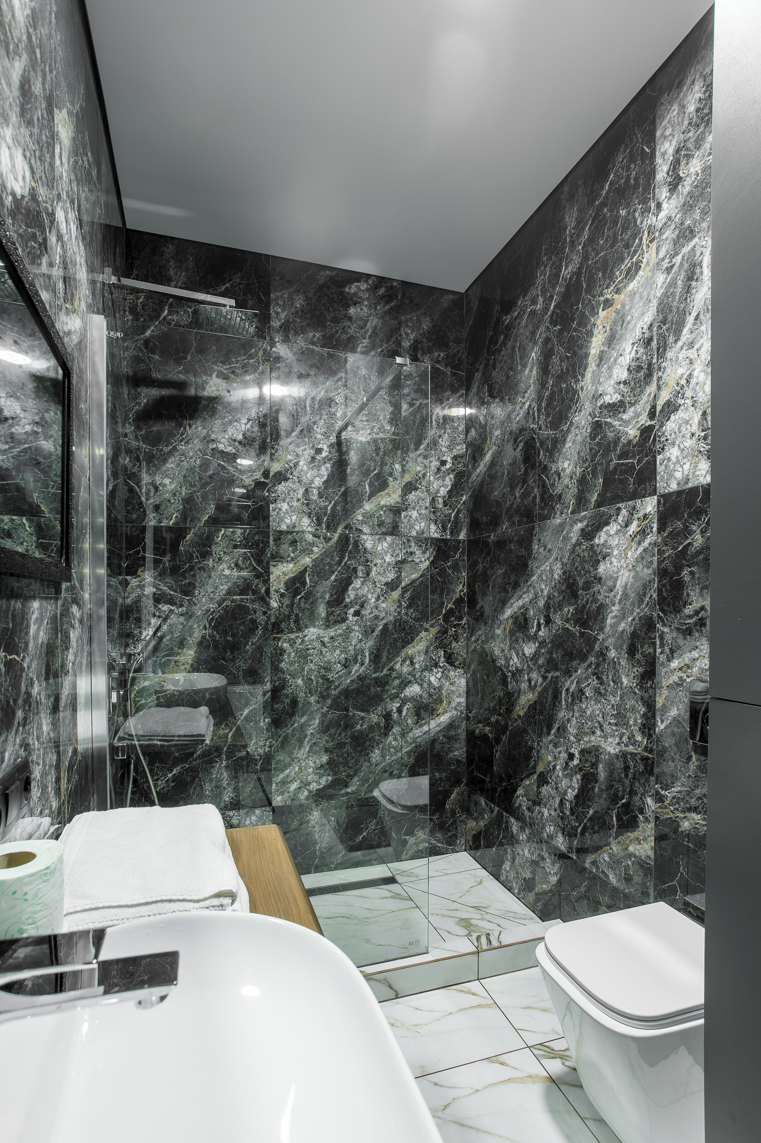 Een moderne badkamer met een marmeren spatwand, een douchecabine van glas en een witte wastafel.