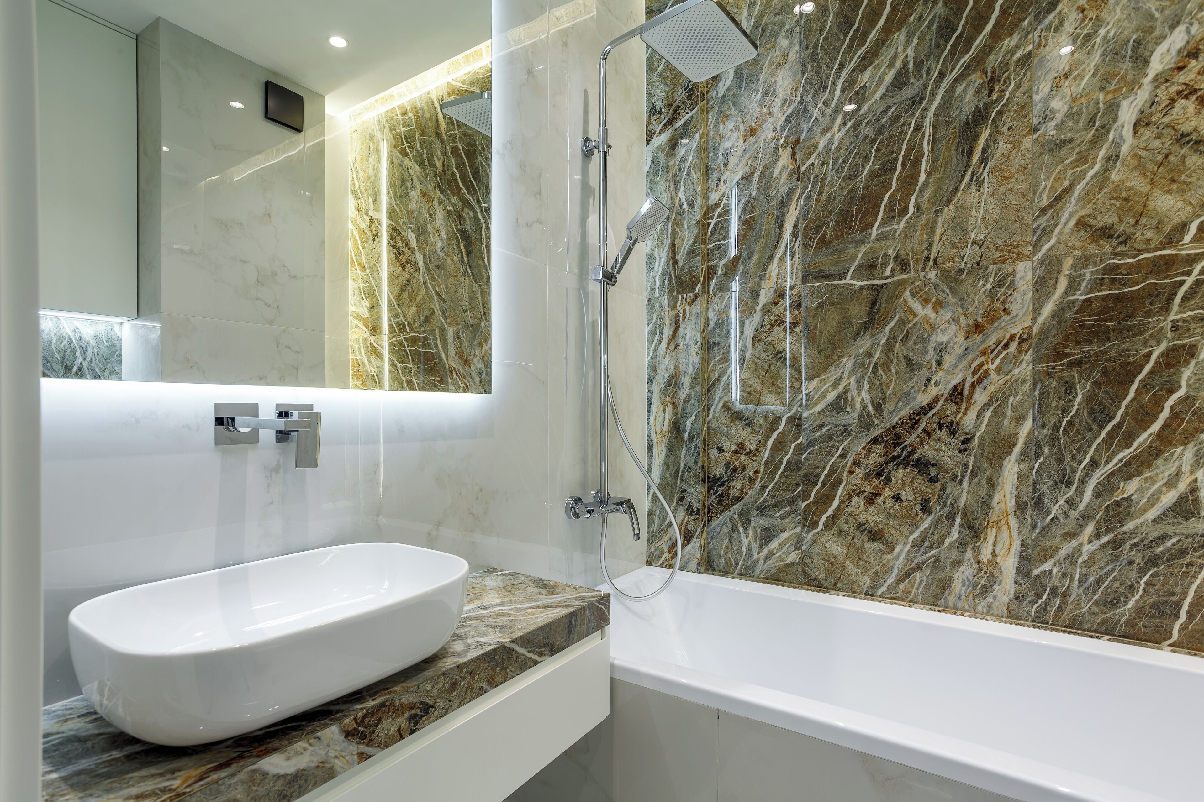 Un baño moderno con pared de mármol, una bañera blanca y un lavabo con encimera de mármol.