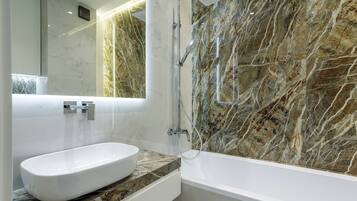 Un baño moderno con pared de mármol, una bañera blanca y un lavabo con encimera de mármol.