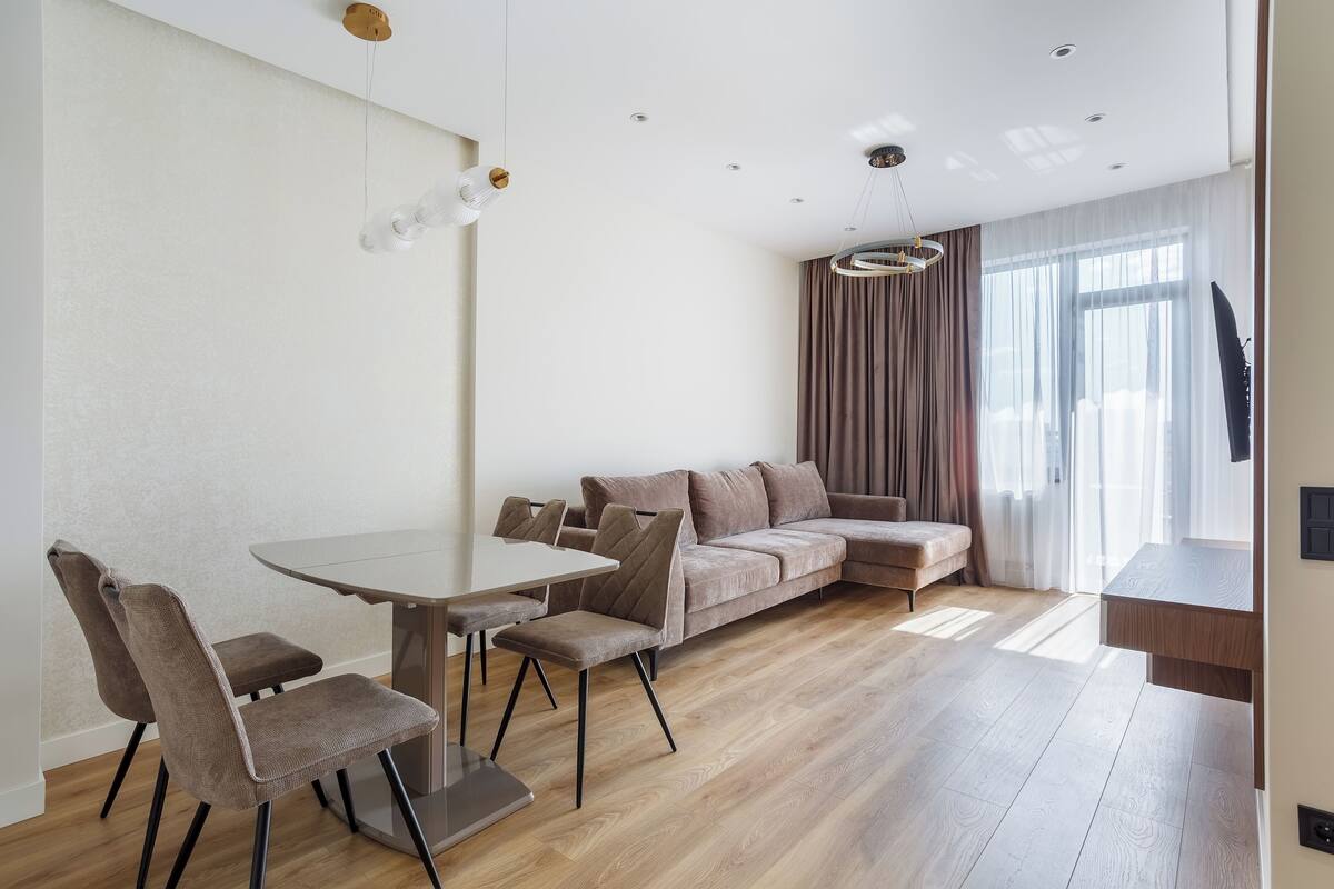 A modern living room with a dining area, a sofa, and a TV mounted on the wall.