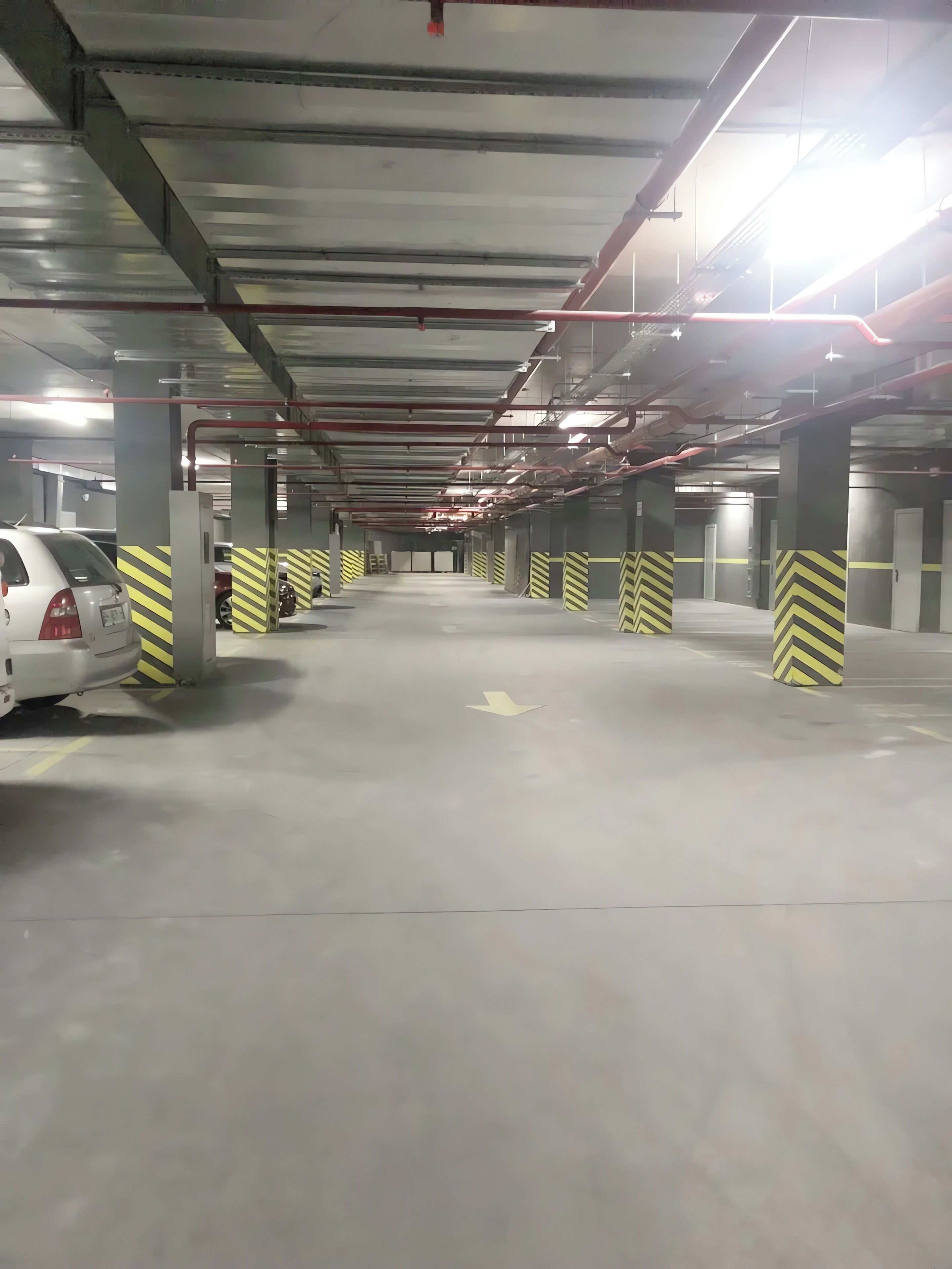 An indoor parking garage with multiple levels, concrete pillars, and directional arrows on the floor.