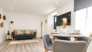 A modern living room with a grey sofa, a dining table with chairs, and a flat-screen TV mounted on the wall. - Klysa (Camborne)