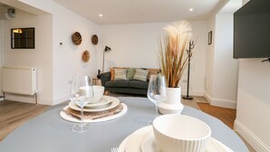 A modern living room with a dining table set for two, a sofa, and a TV mounted on the wall. - Klysa (Camborne)