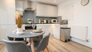 A modern kitchen with grey cabinets, a stainless steel range hood, a microwave, and a small trash bin. - Klysa (Camborne)