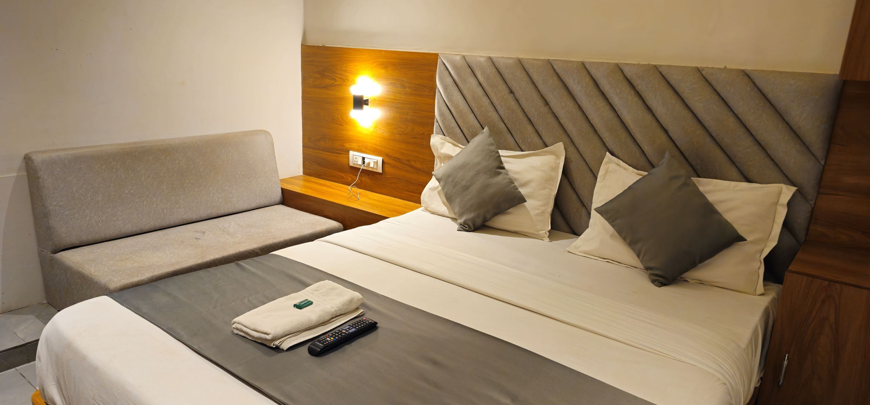 Habitación de hotel con cama, mesita de noche, control remoto y toalla.