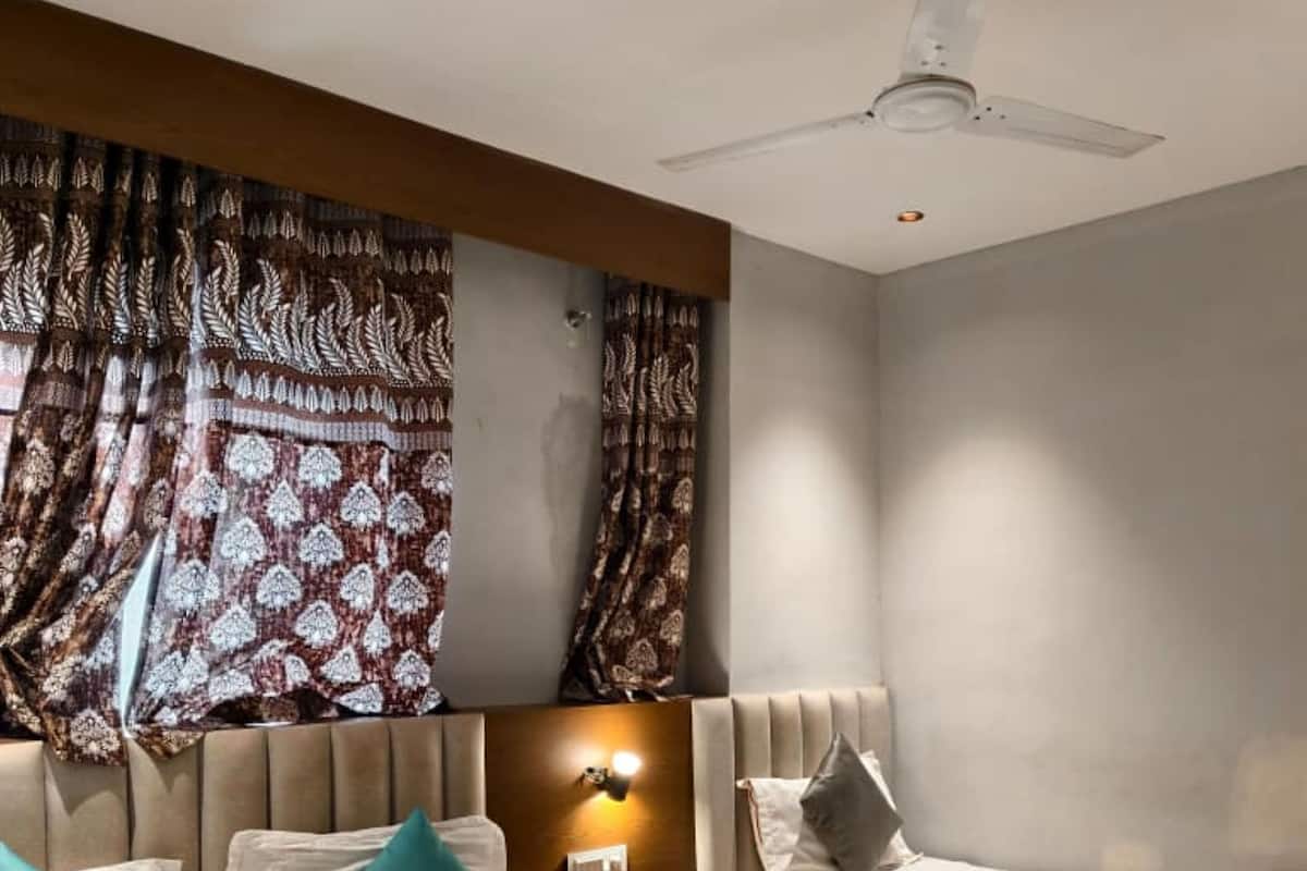 A hotel room with a large bed, two bedside tables, a ceiling fan, and patterned curtains.