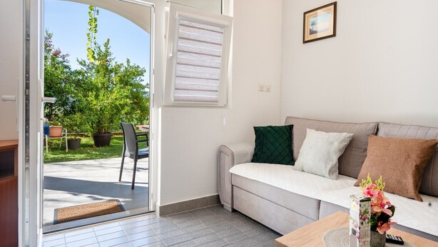 Ein modernes Wohnzimmer mit Sofa, Couchtisch und Blick auf einen Garten durch eine geöffnete Tür.