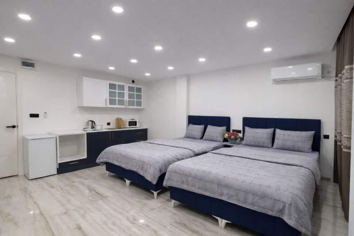 A modern bedroom with two beds, a white wardrobe, a desk, and an air conditioning unit.