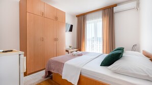 A bedroom with a bed, a wardrobe, a desk, a TV, and a window with curtains.