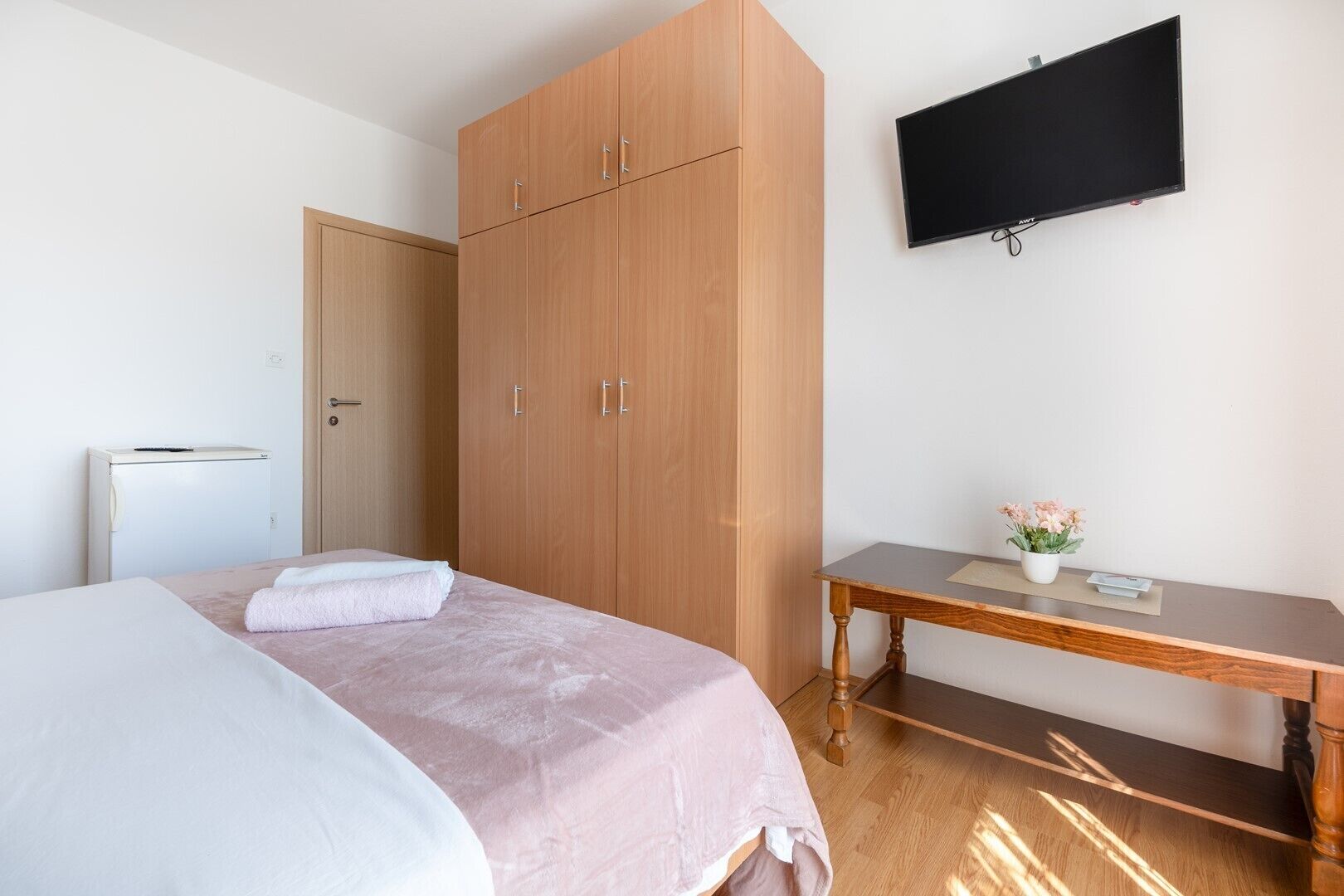 A bedroom with a bed, a wardrobe, a desk, and a TV.