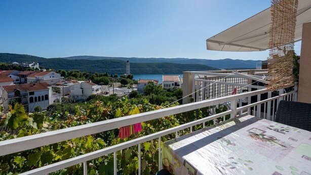 A balcony with a view of a coastal town, a clear sky, and a distant mountain range.