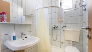 A bathroom with a white sink, toilet, and shower. There is a window above the shower, and a towel rack is visible.