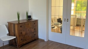 A room with a wooden dresser, a white chair, and a glass door leading outside. - Bright and lovingly furnished vacation apartment with a feel-good atmosphere (Hamm)