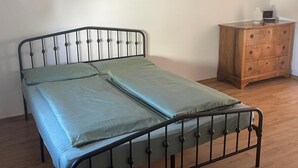 A single bed with a metal frame and a wooden dresser in a room with wooden flooring and white walls. - Bright and lovingly furnished vacation apartment with a feel-good atmosphere (Hamm)