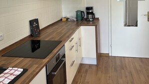 A modern kitchen with white cabinets, a stainless steel range hood, a black induction cooktop, a coffee maker, and a small oven. - Bright and lovingly furnished vacation apartment with a feel-good atmosphere (Hamm)