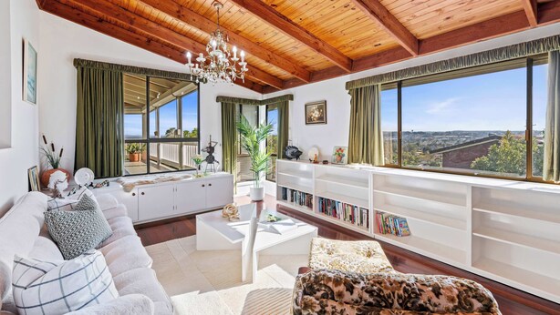 Un salon spacieux avec un plafond haut, de grandes fenêtres, un canapé blanc, une table basse et une bibliothèque.
