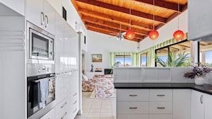 Une cuisine moderne avec des meubles blancs, un four encastré et un ventilateur de plafond.