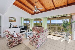 A spacious living area with a ceiling fan, a sofa set, a TV, and a balcony with a view.