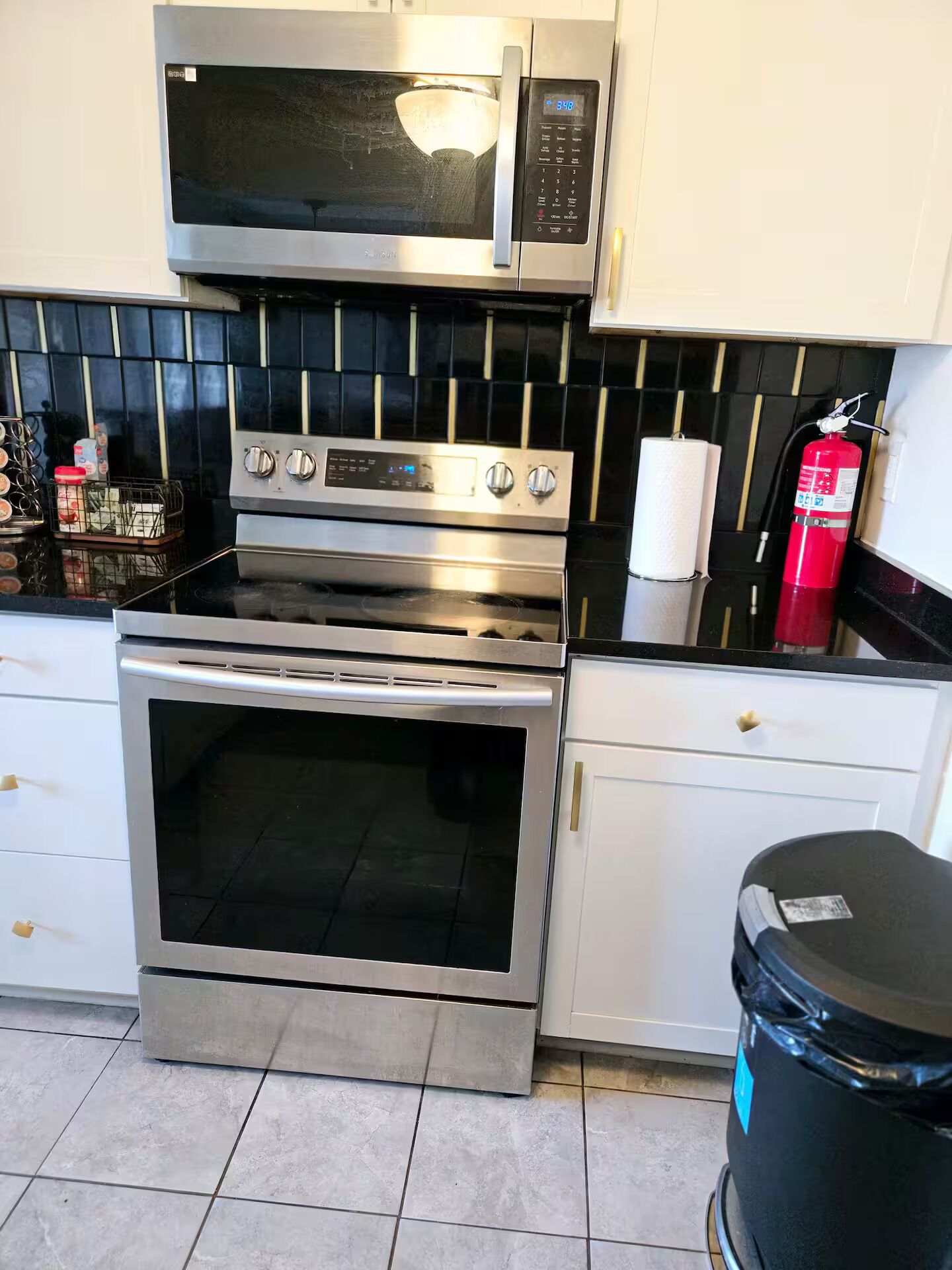 A kitchen with a microwave, oven, and a trash bin.