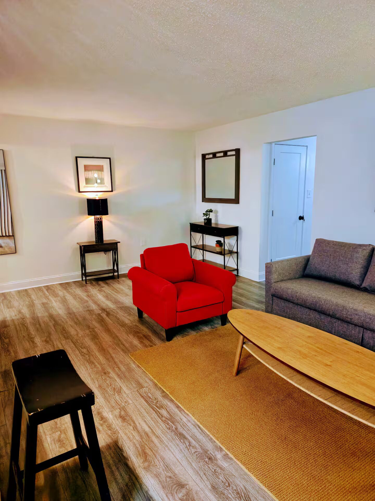 A living room with a red sofa, a grey sofa, a wooden coffee table, a black side table, a lamp, and a framed picture on the wall.