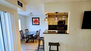 A spacious living area with a dining table and chairs, a kitchen with modern appliances, and a large window with blinds. - Full apartment, 7 minutes from dulles airport (Herndon)
