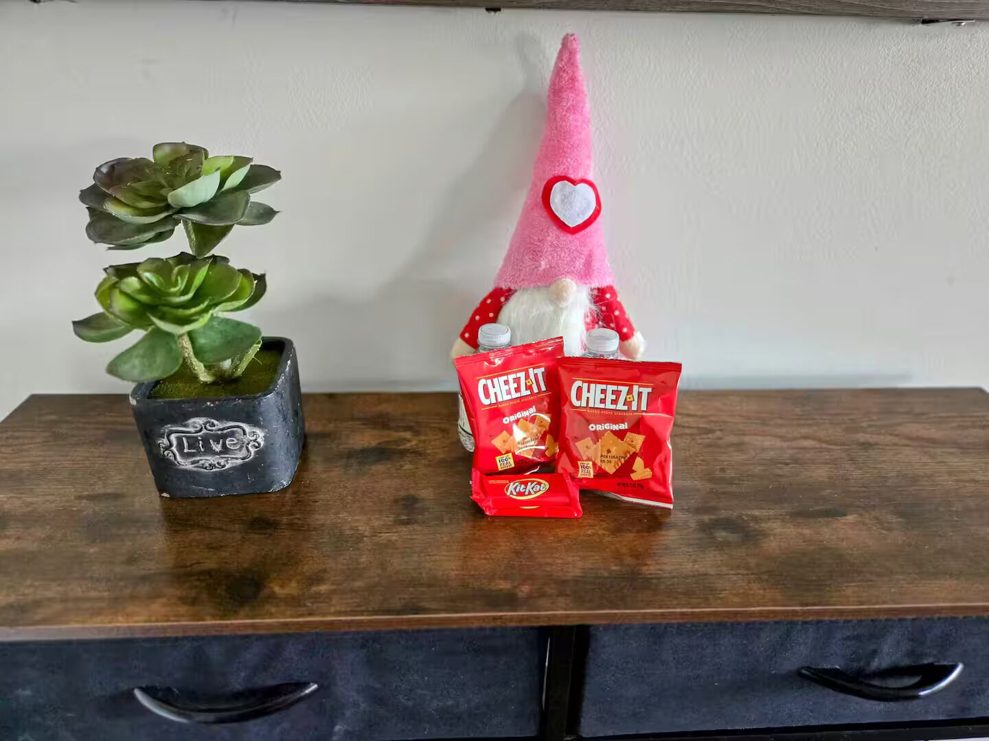 Une table en bois sur laquelle sont posés un pot contenant une plante succulente, une figurine de gnome et deux paquets de crackers Cheez-It.