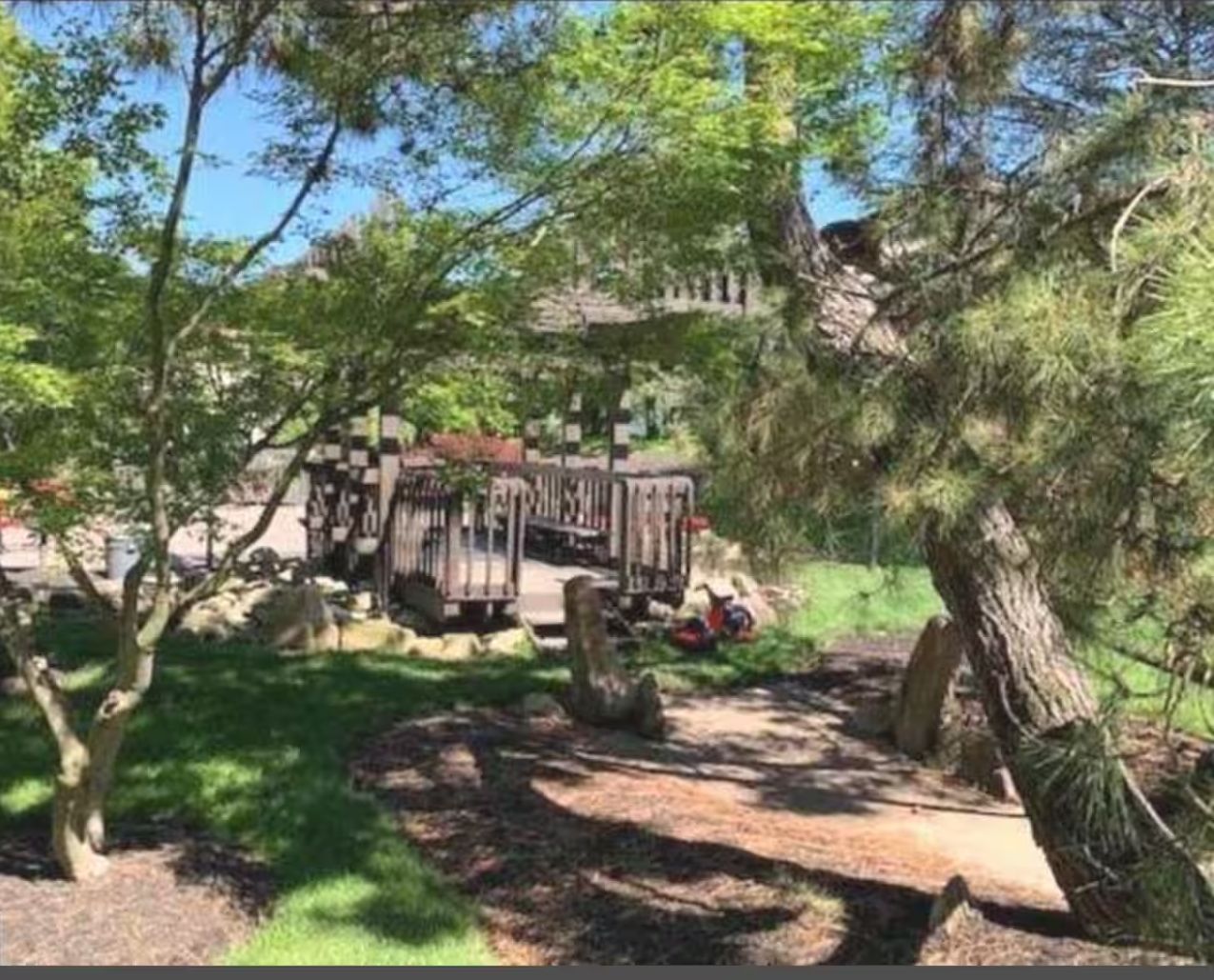 Ein Park mit einer Holzbrücke, Bäumen und einem Gebäude im Hintergrund.