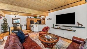 A spacious living area with a wooden ceiling, leather sofas, a round coffee table, and a kitchen in the background.