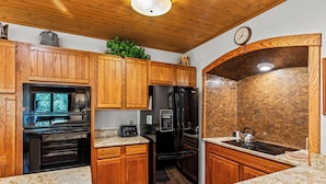 A kitchen with wooden cabinets, granite countertops, a stainless steel sink, a refrigerator, a microwave, and a brick backsplash.