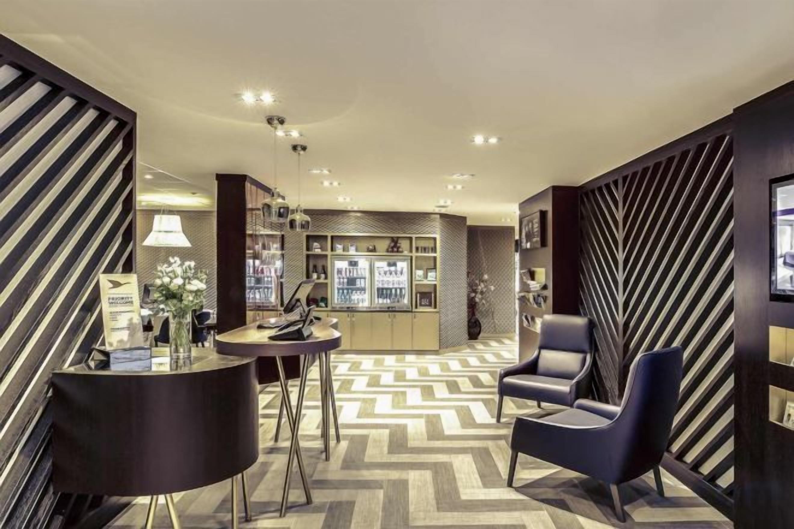 Un moderno vestíbulo de hotel con suelo de diseño geométrico, una recepción, zona de estar y un bar.