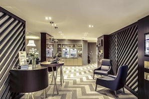 Un moderno vestíbulo de hotel con suelo de diseño geométrico, una recepción, zona de estar y un bar.