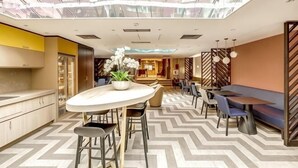 Un moderno vestíbulo de hotel con una mesa redonda central, zona de estar y vistas a la ciudad a través de amplias ventanas.