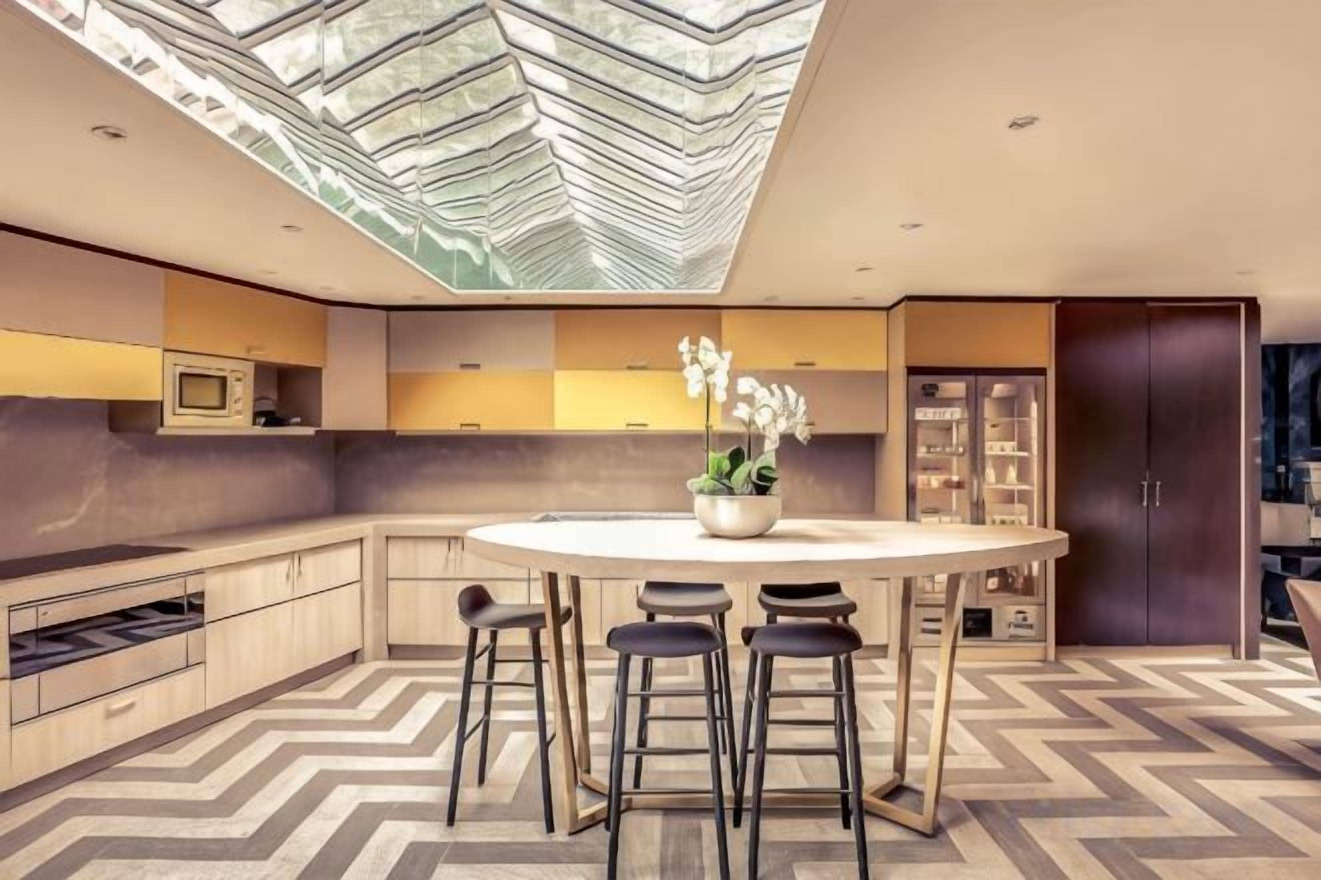 Una cocina moderna con una isla central, taburetes de bar y un ventanal grande.