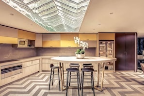 A modern kitchen with a central island, bar stools, and a ceiling skylight.
