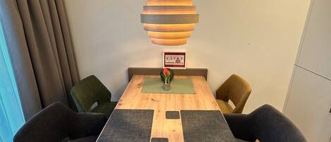 Ein Essbereich mit Holztisch, vier Stühlen und einer hängenden Pendelleuchte.