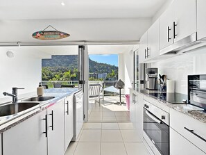 A modern kitchen with a view to a balcony, stainless steel appliances, and a hanging sign. - Beachside 17 (Nelly Bay)