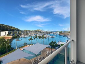 A marina with boats, a pool area with lounge chairs, and a view of buildings in the background. - Beachside 17 (Nelly Bay)
