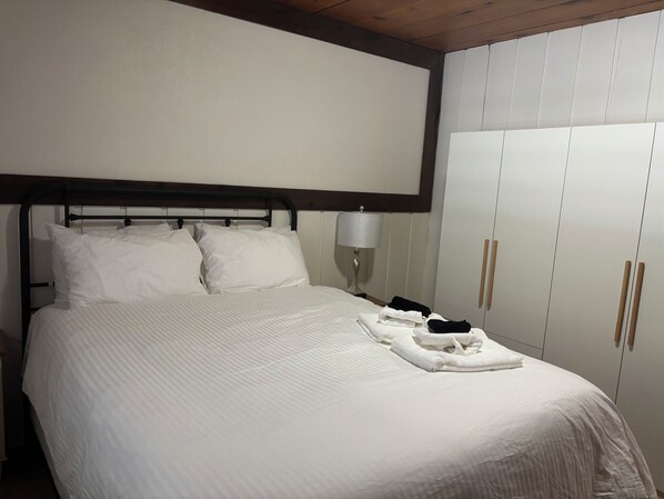 A neatly made bed with white linens and pillows, a bedside lamp, and a wardrobe with wooden handles.